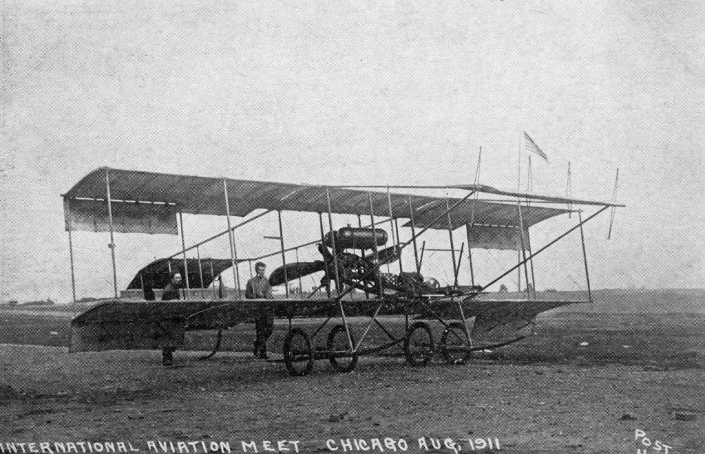 A biplane being walked by a pilot and mechanic.
